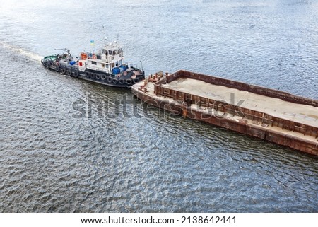 A river tug slowly pushes an empty rusty barge down the river against the backdrop of water ripples. The concept of river freight transport. Copy space.