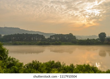 River Under Early Morning Cloud Cover With Thin Layer Of Mist On Water. 