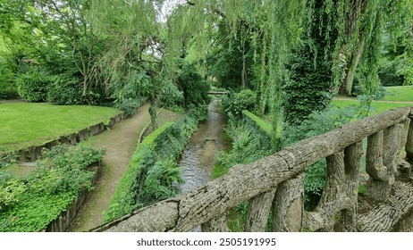 A river view from an old stone bridge, showing the flowing water beneath. The scene includes lush greenery along the riverbanks and the stone railings of the bridge in the foreground. - Powered by Shutterstock