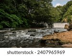 A river and waterfall meandering through Burrs Country Park in Bury, England.