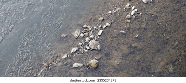 The riverbed is covered in small rocks and pebbles. The water is shallow and clear, and you can see the rocks through the water. - Powered by Shutterstock