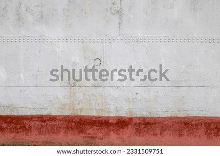 Riveted with button-head rivets metal plate - side of a sea vessel - painted in white with red waterline as an industrial background