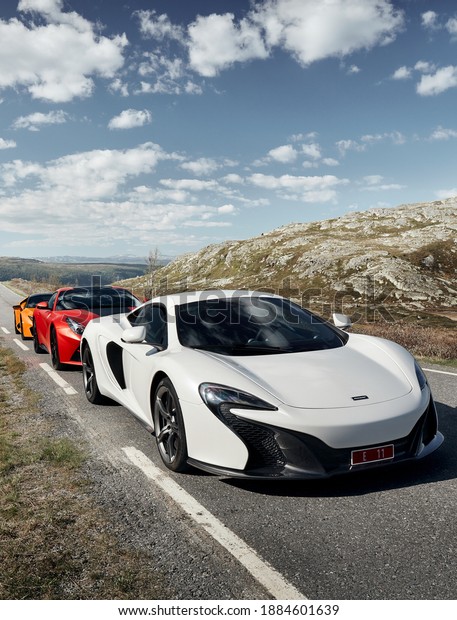 Rjukan, Norway -04.06.2016: White Mclaren 650s,\
Red Ferrari f12 and Yellow Lamborghini Huracan. Three super cars\
stopped for a while in a journey through the mountains of Norway in\
an empty valley.