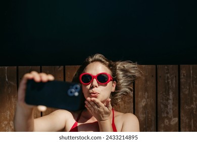 Rlaxed woman blowing kiss, taking selfie when lying on a pier by natural lake in summer - Powered by Shutterstock