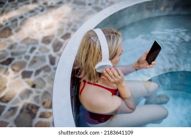Rlaxed woman wearing headphones listening to music and sittin in hot tub, summer vacation concept.