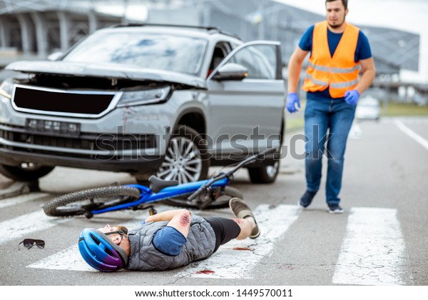 Road accident with injured cyclist lying on\
the pedestrian crossing near the broken bicycle and car driver\
running on the background