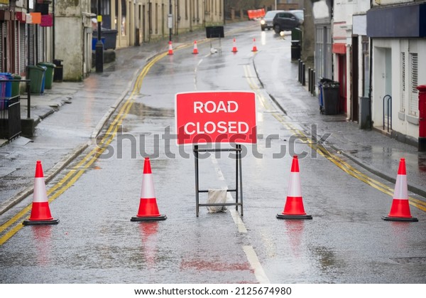 Road ahead closed sign with traffic cones and\
red barrier fence crossing