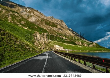 Road among small alpine lake and mountains under stormy cloudy sky near Colle della Maddalena in Italy.