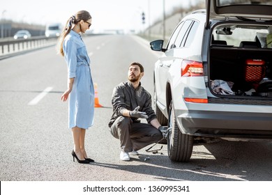 Road Assistance Worker Helping Young Woman To Change A Car Wheel On The Highway