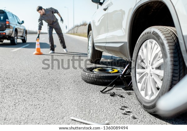 Road assistance worker putting emergency\
cones near the broken car on the\
highway
