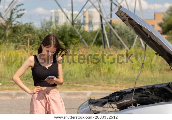 road
assistance,teenager with a broken auto with a mobile phone on the
road is upset with an open hood, waiting for
help