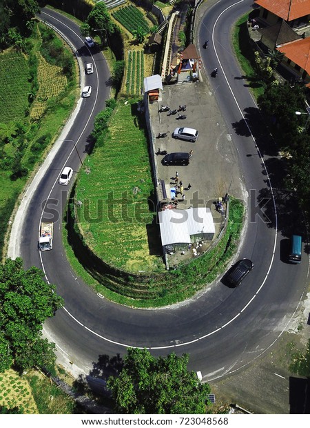 The road is bent by a\
loop, rice fields, cars, roofs of houses. The photo was taken from\
the drone.