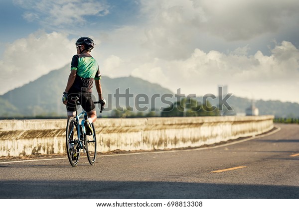 Road bike cyclist man cycling. Biking Sports\
fitness athlete riding bike on an open road to the sunset. Cyclist\
biking on road bike with sun flare. Active healthy sports lifestyle\
athlete cycling.