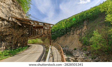 Road with a bridge over a river. The bridge is old and rusted. The road is narrow and winding. The bridge is the only way to cross the river