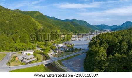 Road by Japanese house and flooded rice fields in green valley landscape