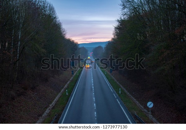 Road with cars fenced by trees in the evening\
with twilight