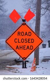 Road Closed Sign In Front Of A Snowy Road As Snow Is Still Falling