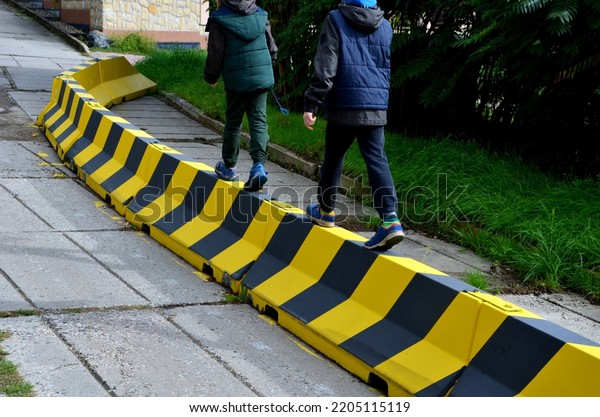 road concrete barriers road narrowing\
with yellow and black striping. Two boys learn stability on the\
obstacle. they balance on the upper edge of the\
barrier