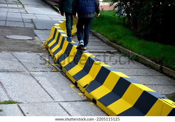 road concrete barriers road narrowing\
with yellow and black striping. Two boys learn stability on the\
obstacle. they balance on the upper edge of the\
barrier
