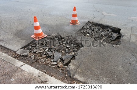 Road construction, road rehabilitation, asphalting.
Holes and damage on an asphalt road, secured by red and white shut-off cones because of the risk of accidents
