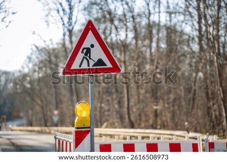 Road construction warning sign with illuminated safety light, work zone hazard alert, red and white striped barricade for traffic control and pedestrian safety