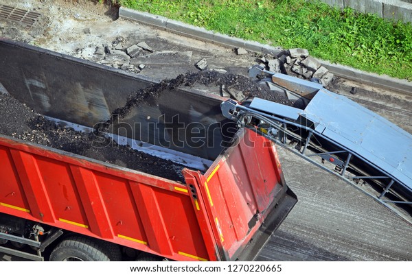 Road\
construction work. Shredded removed the old asphalt pours from the\
conveyor belt road milling machine in a truck\
dump\
