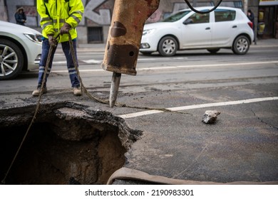 Road construction worker with machines repair Huge sinkhole on busy asphalt road surface on which cars drive. Accident situation on a city street due to cracks in asphalt. Broken hole. - Shutterstock ID 2190983301