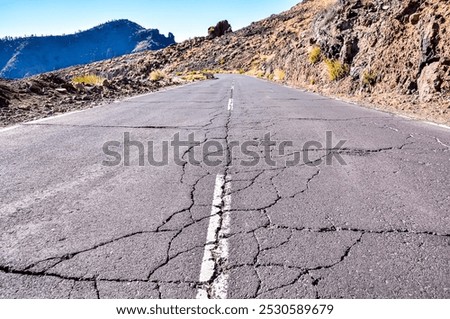 A road with a lot of cracks and potholes. The road is empty and there is no one on it