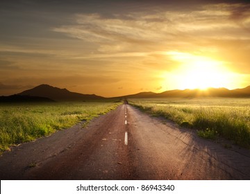 road crosses rural landscape with the silhouette of hill on background the colors of a fiery sunset - Powered by Shutterstock