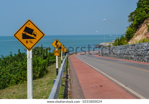 Road curve with caution signs and blue sea\
background Chanthaburi\
Thailand.