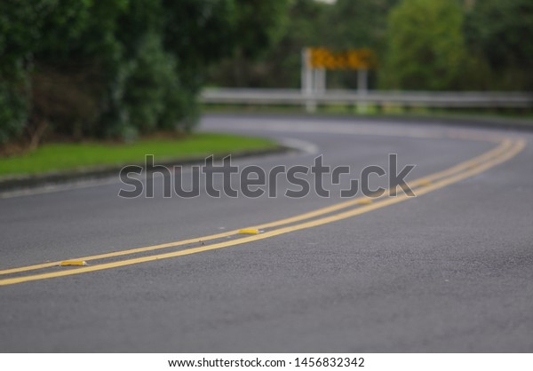 Road curve  \
\
Focusing on the road’s double yellow\
lines with night time reflectors and a burled road sign in the\
background. \
