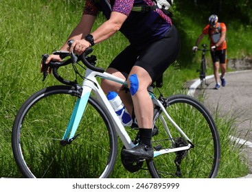 Road cyclist with a patch athletic taping
 on their knee and a cyclist with a flat tire in the background - Powered by Shutterstock