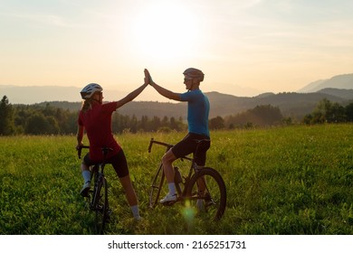 Road cyclists, man and woman, stopping at a grassy hill to celebrate the race achievement with high five gesture, at sunset light. - Powered by Shutterstock