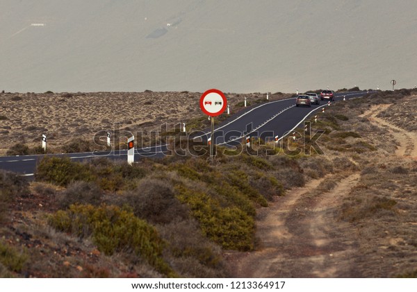 the road in the desert is\
climbing a hill, three cars and the sign of overtaking is\
prohibited