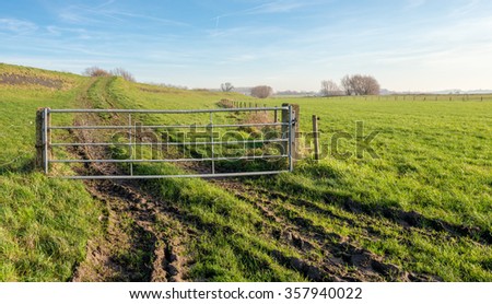 The road to the dike is closed with a galvanized steel gate. Image taken on a sunny day in the autumn season.