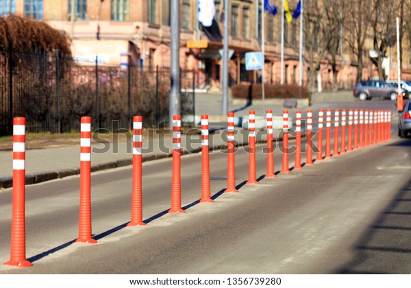 The road is divided by red road columns on the\
background of a city\
street.
