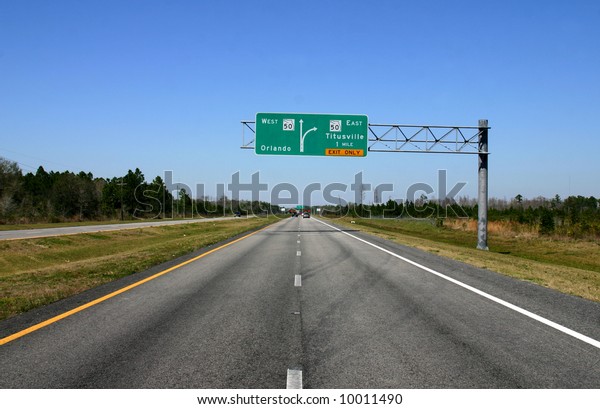 Road fading into Distance with Road sign\
giving directions in\
mid-ground