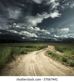 Road in field and stormy clouds