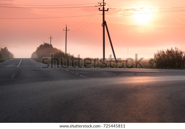 The road in the fog. Red sunrise. Electric poles\
near the road in the\
morning.