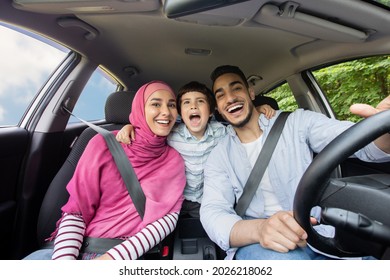 Road Fun. Joyful Muslim Family Of Three Singing Inside Of Car Together, Happy Middle Eastern Dad, Little Son And Mother In Hijab Enjoying Drive Trip Together, Laughing And Looking At Camera, Closeup