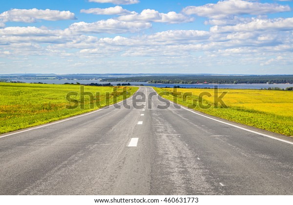 The road goes into the\
distance through the field on a background of a beautiful summer\
landscape