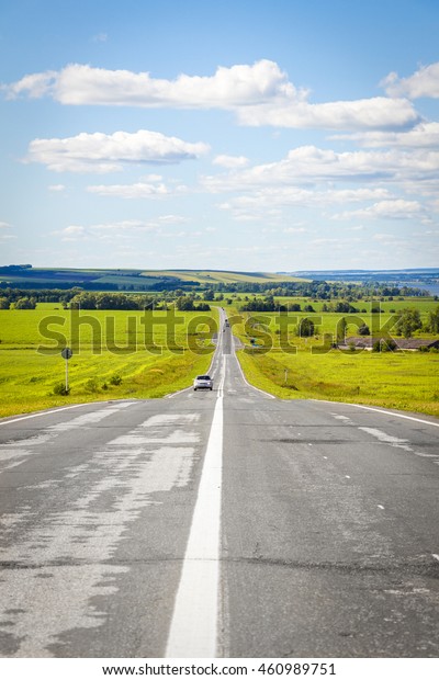 The road goes into the
distance through the field on a background of a beautiful summer
landscape
