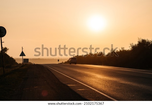 the road going into the distance in the rays of an\
orange sunset