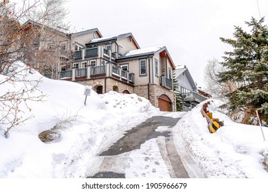 Road Going Up A Snowy Slope Leading To Houses With Cloudy Sky Overhead In Winter