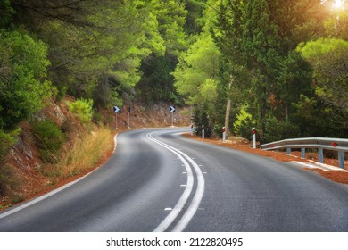 Road in green forest at sunset in summer. Beautiful empty mountain roadway, trees. Colorful landscape with road through the woods in spring. Travel in Greece. Road trip. Transportation. Highway