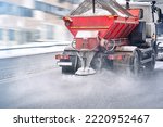 Road and highway maintenance gritter truck spreading de-icing salt on road in winter. Salt spreading. Snow plow service truck removing snow and spreading salt on snowy city road during blizzard