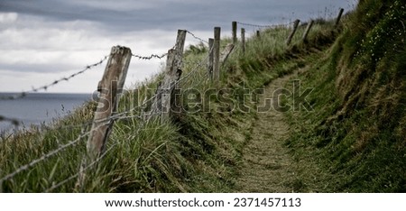 A road up the hill with barbed wire on pieces of wood on the edge, over a background of the Irish sea and a cloudy sky, Ardmore
