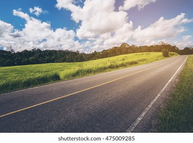 Road Up Hill With Green Grass Under White Clouds And Blue Sky.