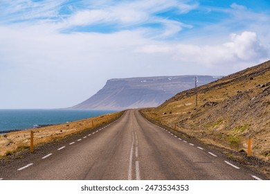 Road in iceland bending around a hill, with high mountains, fjord, sea, blue sky, sunshine, cliffs, on road 60 in the Westfjords - Powered by Shutterstock