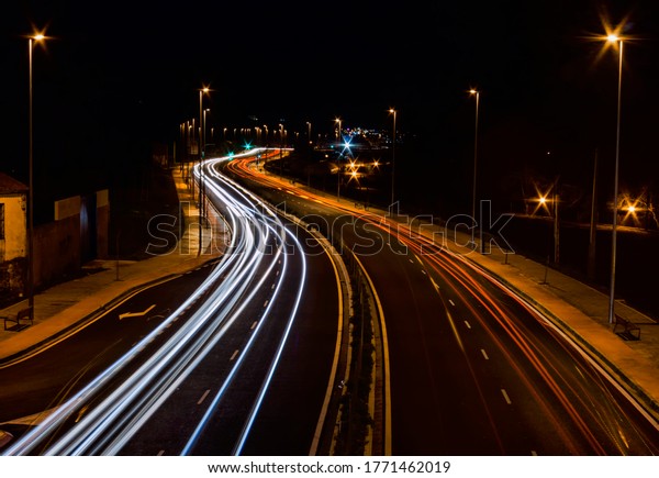Road illuminated by trails of colored lights left by\
cars as they pass